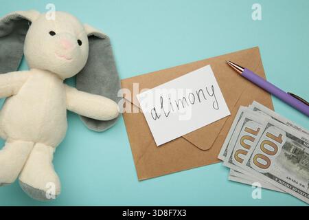 Toy bunny and envelope with word Alimony and money on blue background. Top view Stock Photo