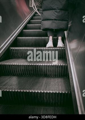 Person standing on an upward-moving escalator, traveling through a modern urban environment Stock Photo