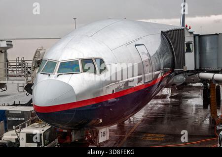 A shiny silver airplane nose stands at the terminal in Madrid, Spain. Rain glistens on its surface as the jet prepares for boarding. Stock Photo