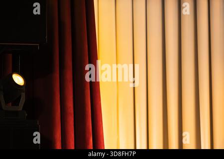 A closeup view of deep red theater curtains beside a bright warm spotlight beam on the right, creating a dramatic stage scene full of anticipation and Stock Photo