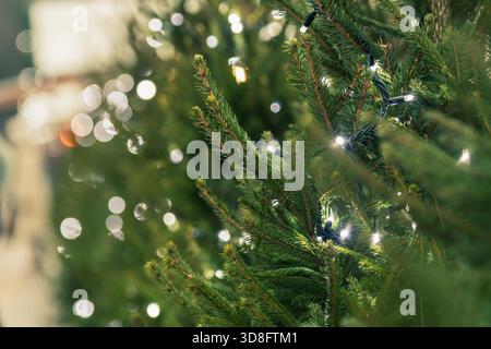 Close-up of a Christmas tree decorated with string lights, featuring soft bokeh illumination and green pine branches Stock Photo