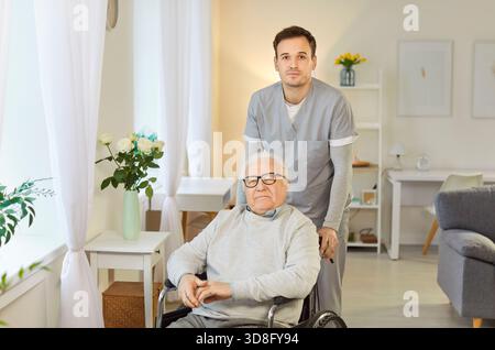 Health care worker in uniform with elderly man in wheelchair standing in rehabilitation clinic. Stock Photo