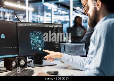 Data center engineering team monitoring system performance using PC, identifying bottlenecks. Server farm teamworking colleagues troubleshooting glitches, implementing optimizations Stock Photo