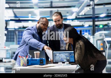 Multiethnic team of technicians collaborating in a solar panel power plant, reviewing blueprints and sharing ideas to enhance renewable energy production and sustainable innovation. Stock Photo