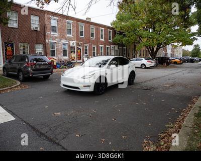 A modern white Tesla Model Y SUV parked on a residential street lined with red brick row houses in New Castle, Delaware. Stock Photo