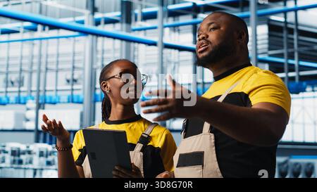 Photovoltaics smart factory staff members using tablet, researching PV materials. Industry 4.0 solar panels plant african american engineers developing alternative energy systems prototypes, camera A Stock Photo