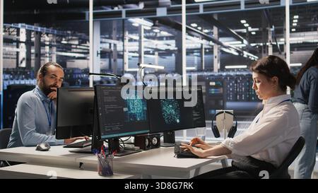 Tired data center engineer stretching, monitoring server clusters performing AI training. Fatigued server farm IT specialist supervising computing systems managing deep learning operations, camera A Stock Photo