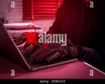 Cybersecurity threat concept showing hacker or scammer using laptop with glowing red unlocked padlock icon, representing hacking, data breach, online Stock Photo