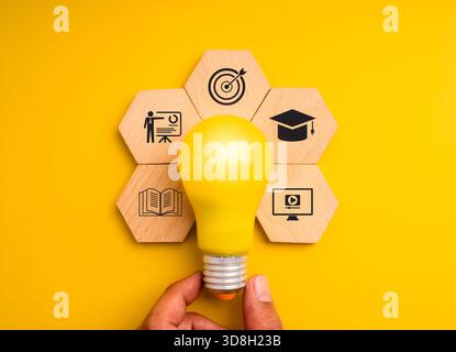 Yellow light bulb with icons of learning, training, and education on hexagon wood blocks symbolizes knowledge, creativity, and e-learning. Ideal for m Stock Photo