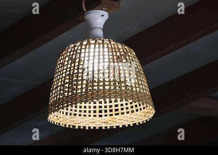 Cozy warm rustic lamp with handmade bamboo wicker light shade. beautiful interior decoration creating an inviting atmosphere hanging from dark ceiling Stock Photo
