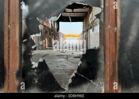 Empty ruins of a very heavily polluted industrial factory, abandoned empty building through burned black broken shattered glass, red stone tile wall Stock Photo