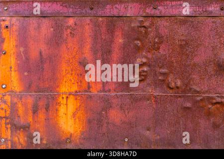Corroded metal sheets fastened with hex screw heads and welded seams, displaying a range of rust tones - full-frame flat background and texture. Stock Photo