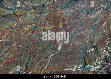 Detailed view of a rough Blue Gold Granite surface showcasing swirling patterns of blue, gold, brown, and gray with visible crystalline structure and natural cracks. Stock Photo