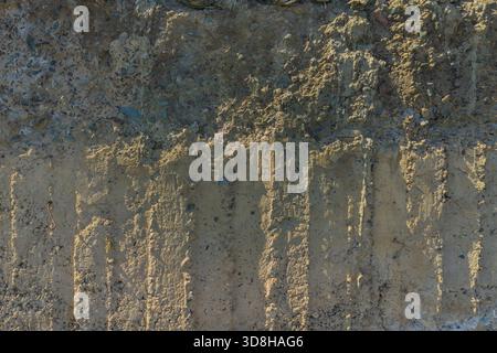 Rough, uneven concrete surface embedded with small pebbles and showing signs of age and wear under tangential harsh sun light showing all imperfections. Stock Photo