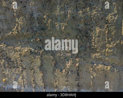 Rough, uneven concrete surface embedded with small pebbles and showing signs of age and wear under tangential harsh sun light showing all imperfections. Stock Photo