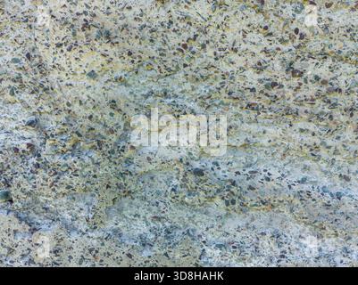 A close-up shows a concrete texture with a high concentration of colorful pebbles and stones exposed on its rough surface. This is a prominent example of exposed aggregate concrete. Stock Photo