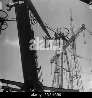 Donetsk region, Ukrainian SSR, Soviet Union. 1970s. A specialized tracked aerial work platform operates at the open switchgear yard of a high-voltage electrical substation. Installers in the basket of the telescopic lift are performing maintenance on massive air blast circuit breakers and porcelain insulators. The heavy crawler chassis allows the machine to maneuver on the rough terrain of the construction site. View through the metal lattice of a transmission tower. Life in peaceful Donbas before the war. Stock Photo