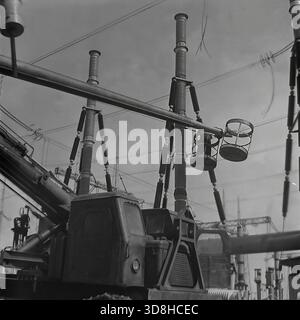 Donetsk region, Ukrainian SSR, Soviet Union. 1970s. A specialized tracked aerial work platform operates at the open switchgear yard of a high-voltage electrical substation. Installers in the basket of the telescopic lift are performing maintenance on massive air blast circuit breakers and porcelain insulators. The heavy crawler chassis allows the machine to maneuver on the rough terrain of the construction site. View through the metal lattice of a transmission tower. Life in peaceful Donbas before the war. Stock Photo