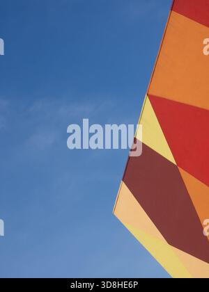Colorful building wall exterior with lines and shapes against a blue sky with some clouds, Stock Photo