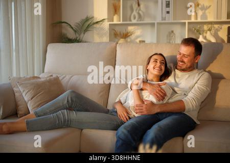 Happy couple in love looking each other at sunset sitting on a couch at home Stock Photo