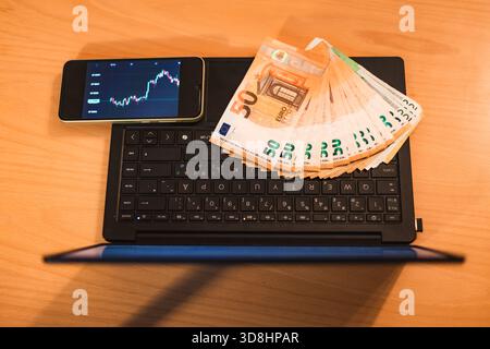Close-up photo of hands holding euro banknotes while using a laptop and smartphone showing cryptocurrency charts. Perfect for fintech, crypto trading, Stock Photo