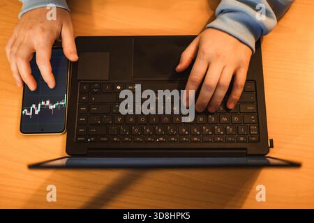 Photo of hands typing on a laptop with cryptocurrency charts displayed on the screen. Close-up showing keyboard and graphs, ideal for fintech, digital Stock Photo