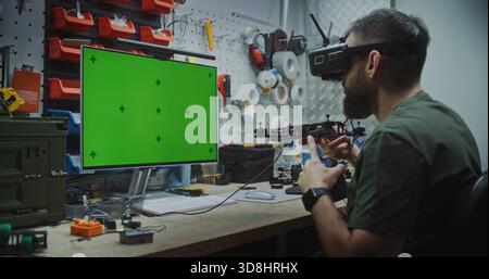 Engineer Building Drone With Dedicated Computer Display. Focused Man Working in Technical Workshop. Man Building Drone With Unedited Green Screen Monitor Used For Displaying Schematics or Software. Stock Photo