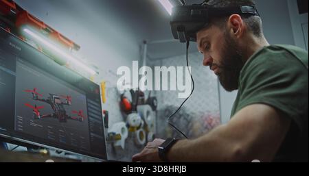 Bearded Man in Tactical Gear Deeply Focused, Using Computer Display and FPV Gear While Working on Drone Electronics. Engineer Utilizing Digital and Physical Tools. Dedication to Military Grade Tech. Stock Photo
