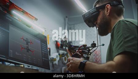 Bearded Man in Tactical Gear Deeply Focused, Using Computer Display and FPV Gear While Working on Drone Electronics. Engineer Utilizing Digital and Physical Tools. Dedication to Military Grade Tech. Stock Photo