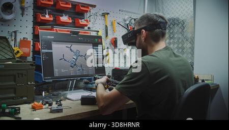 Man Designing and Assembling Drones. Engineer Wearing FPV Goggles Simultaneously Designing Drone on Screen and Assembling Workbench. Concept of Advanced Research and Development in Drone Technology. Stock Photo
