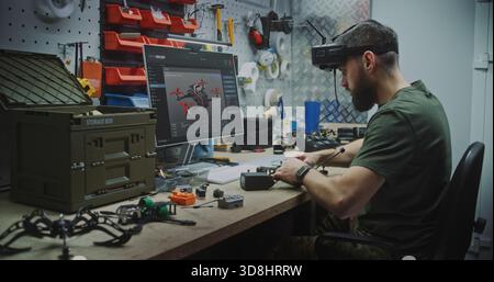 Engineer Using VR Goggles to Virtually Design. Man in Military Style Uniform Utilizing VR Goggles and Computer While Assembling Drone Components. Concept Integration of Virtual Tools in Engineering. Stock Photo