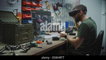 Engineer Using VR Goggles to Virtually Design. Man in Military Style Uniform Utilizing VR Goggles and Computer While Assembling Drone Components. Concept Integration of Virtual Tools in Engineering. Stock Photo
