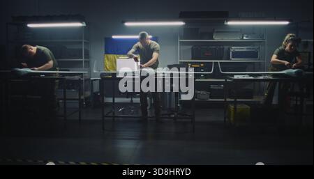Busy Team of Specialists Meticulously Assembles Unmanned Aerial Vehicle and Movement of Equipment in Workshop Under Ukrainian Flag. Concept of National Effort in High Tech Defense Production. Stock Photo