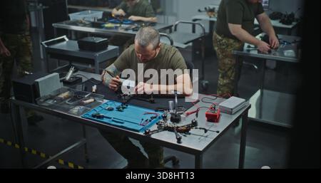 Technician Performing Intricate Repair and Maintenance FPV Drone Electronics, Using Soldering Iron. Concept of Technical Service and Complexity of Drone Maintenance, Troubleshooting, Refining drone. Stock Photo