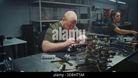 Busy, Well Lit Tech Workshop Shows Multiple Engineers Immersed in Drone Development. Concept of Collaboration, Innovation, and Intense Focus Required For Cutting Edge Electronics Production. Stock Photo