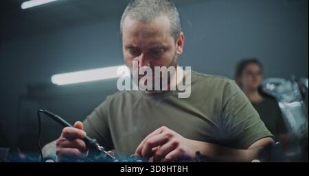 Close Up Skilled Worker Soldering Components in Modern Drone Manufacturing Facility. Man Using Soldering Iron Connects Small Parts Drone Core on Workbench. Detailed Manufacturing, Hands on Production. Stock Photo
