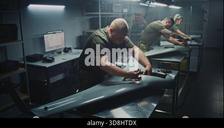Installing Flight Electronics Technician Working on UAVs Core. Team in Uniform Installing or Checking Complex Flight Electronics Inside Body of UAV. Precision Required For Military Drone Systems. Stock Photo