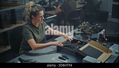 Female Engineer Assembling FPV Drone For Defense or Security Purposes. Focused Woman Meticulously Assembling Drone in Manufacturing Facility. Concept Women Role in Technology and Defense Production. Stock Photo