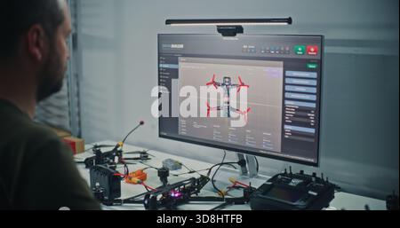 Male Engineer With Visible Tattoos Sits at Computer, Designing FPV Drone Model Using Specialized 3D Software For Drone Testing. Concept Technical Process Product Development and Digital Engineering. Stock Photo