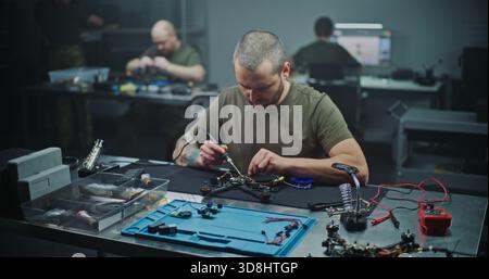 Technician Soldering Components on FPV Drone Circuit Board. Man Carefully Soldering Tiny Electronic Components Onto Small Circuit Board, Part of Drone. Precise Electronic Assembly in Modern Workshop. Stock Photo