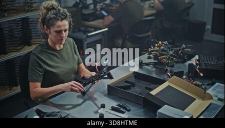 Female Engineer Assembling FPV Drone For Defense or Security Purposes. Focused Woman Meticulously Assembling Drone in Manufacturing Facility. Concept Women Role in Technology and Defense Production. Stock Photo