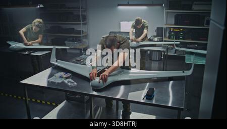 Woman and Men Assembling Advanced Military Drones in Factory. Woman Engineer Works Alongside Male Colleagues, Assembling Advanced Military Drones in Modern Factory Setting. Defense Manufacturing. Stock Photo