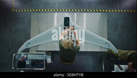 Woman in Camouflage Uniform Working on Next Generation Drone. Female Soldier Installing Electronic Parts Into Surveillance Drone. Concept of Advanced Military Research and Development. Top View. Stock Photo