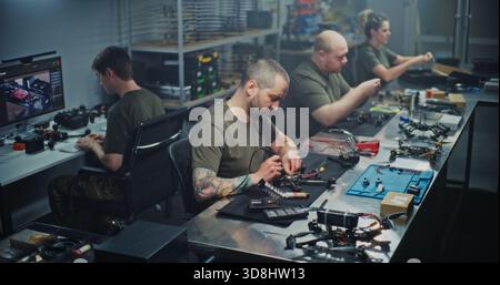 Engineers Collaborating on FPV Drone Production in Modern Workshop. Diverse Team Works Collaboratively Assembling and Calibrating FPV Drones. Concept of Efficient Teamwork in High Tech Manufacturing. Stock Photo