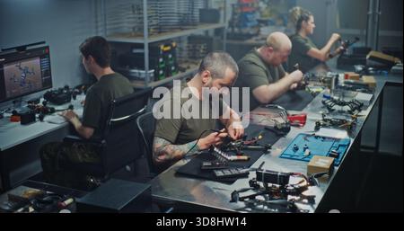Engineers Collaborating on FPV Drone Production in Modern Workshop. Diverse Team Works Collaboratively Assembling and Calibrating FPV Drones. Concept of Efficient Teamwork in High Tech Manufacturing. Stock Photo