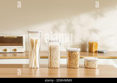 Row of clear plastic airtight food containers filled with spaghetti oats and soybeans on kitchen counter with copy space Stock Photo