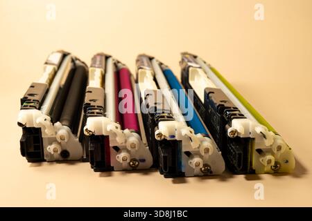 Four color printer cartridges arranged in a row on a beige background represent printing supplies, maintenance, and office service Stock Photo