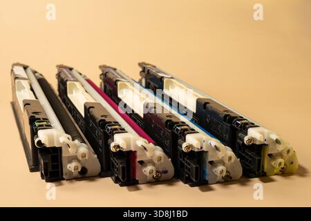 Four color printer cartridges arranged in a row on a beige background represent printing supplies, maintenance, and office service Stock Photo