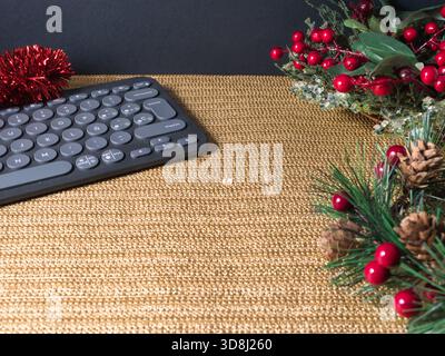 Festive Workspace Christmas Theme - Modern keyboard on a golden desk with festive Christmas decorations: red berries, pinecones, and tinsel. Ideal for Stock Photo