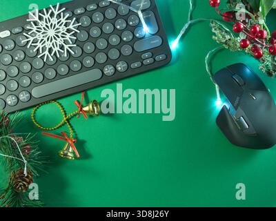Festive Work Setup with Keyboard - Flat lay of a computer keyboard adorned with Christmas decorations and fairy lights on a vibrant green background, Stock Photo